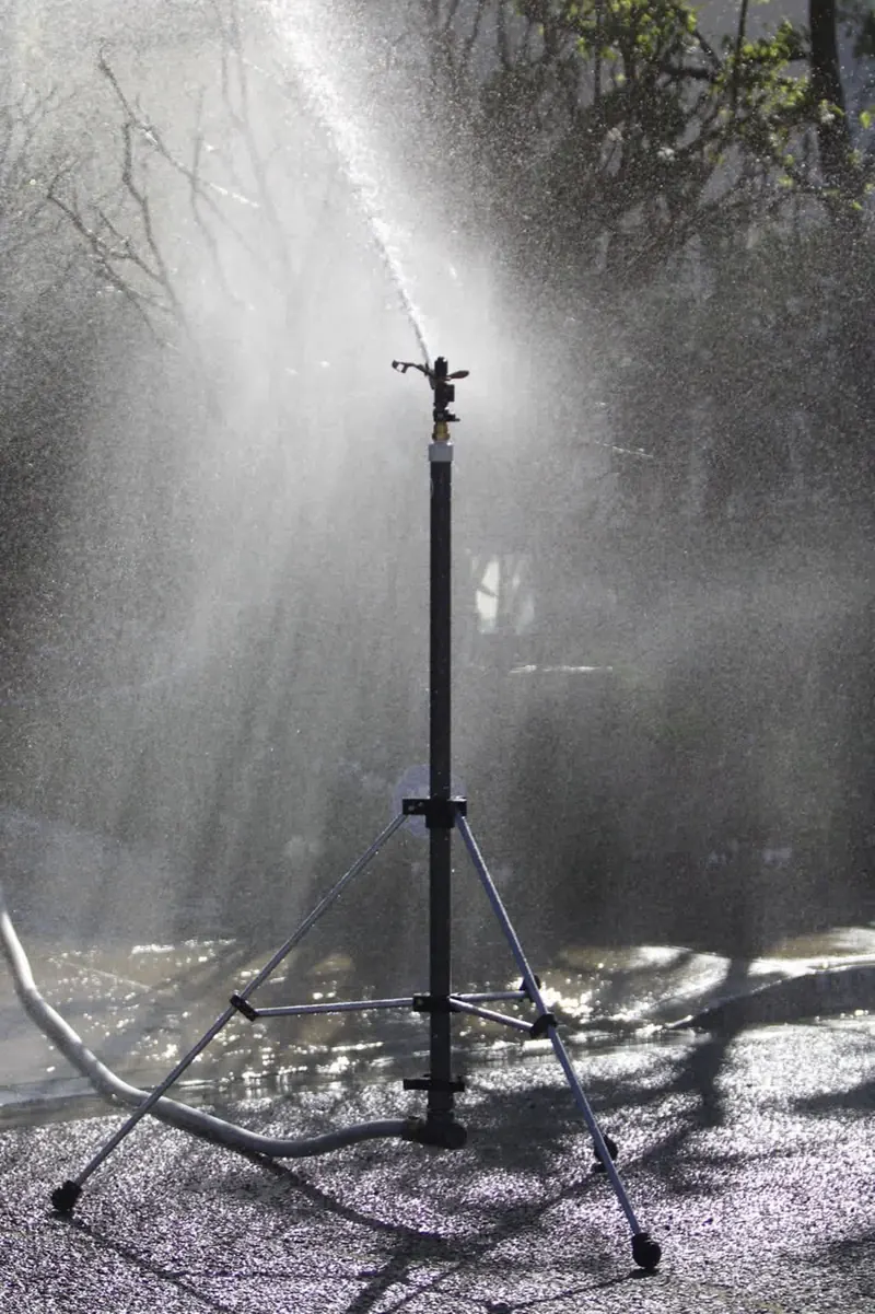 An attack tripod sprinkler spraying in a yard