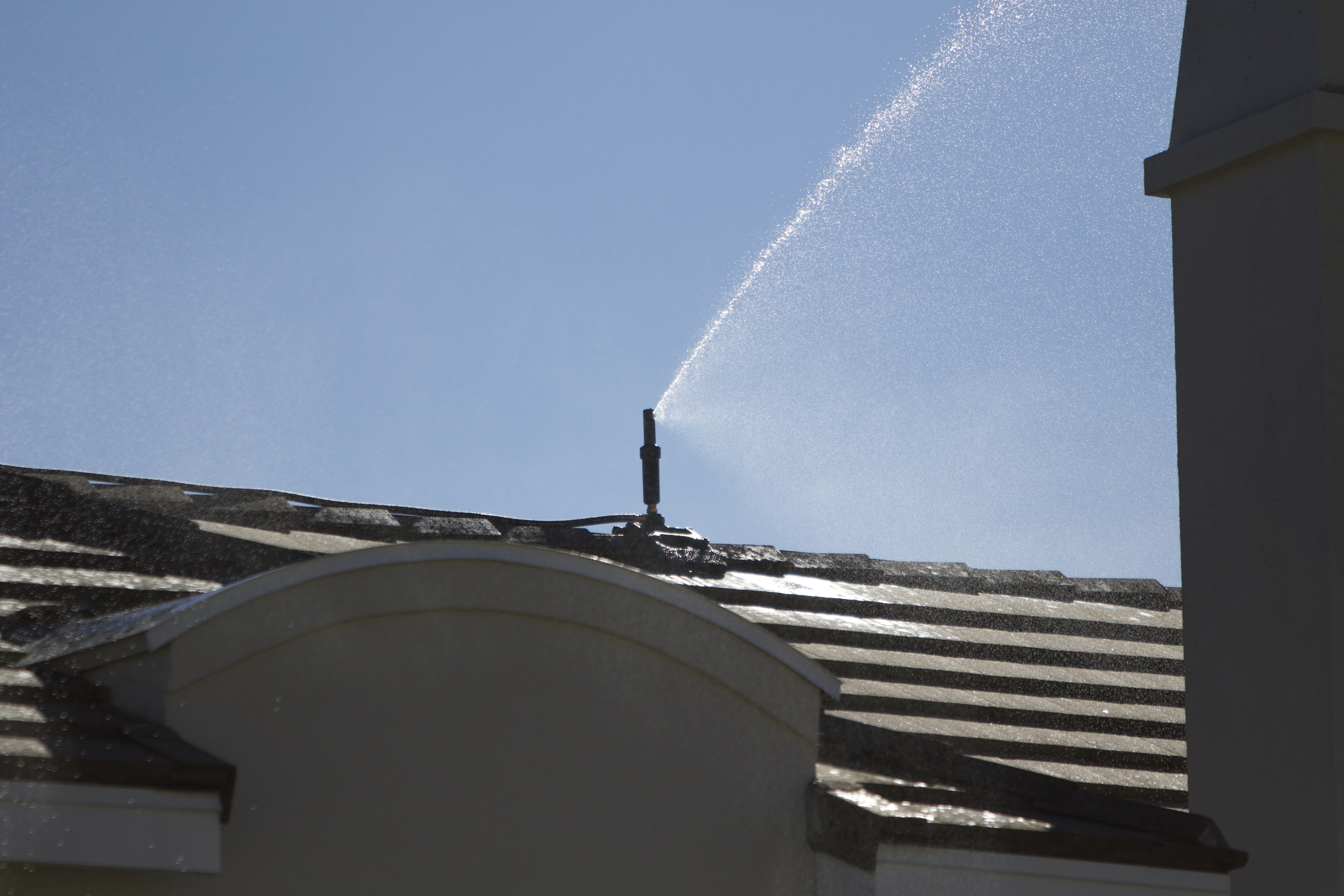 Roof sprinkler actively pre-wetting a home's roof line