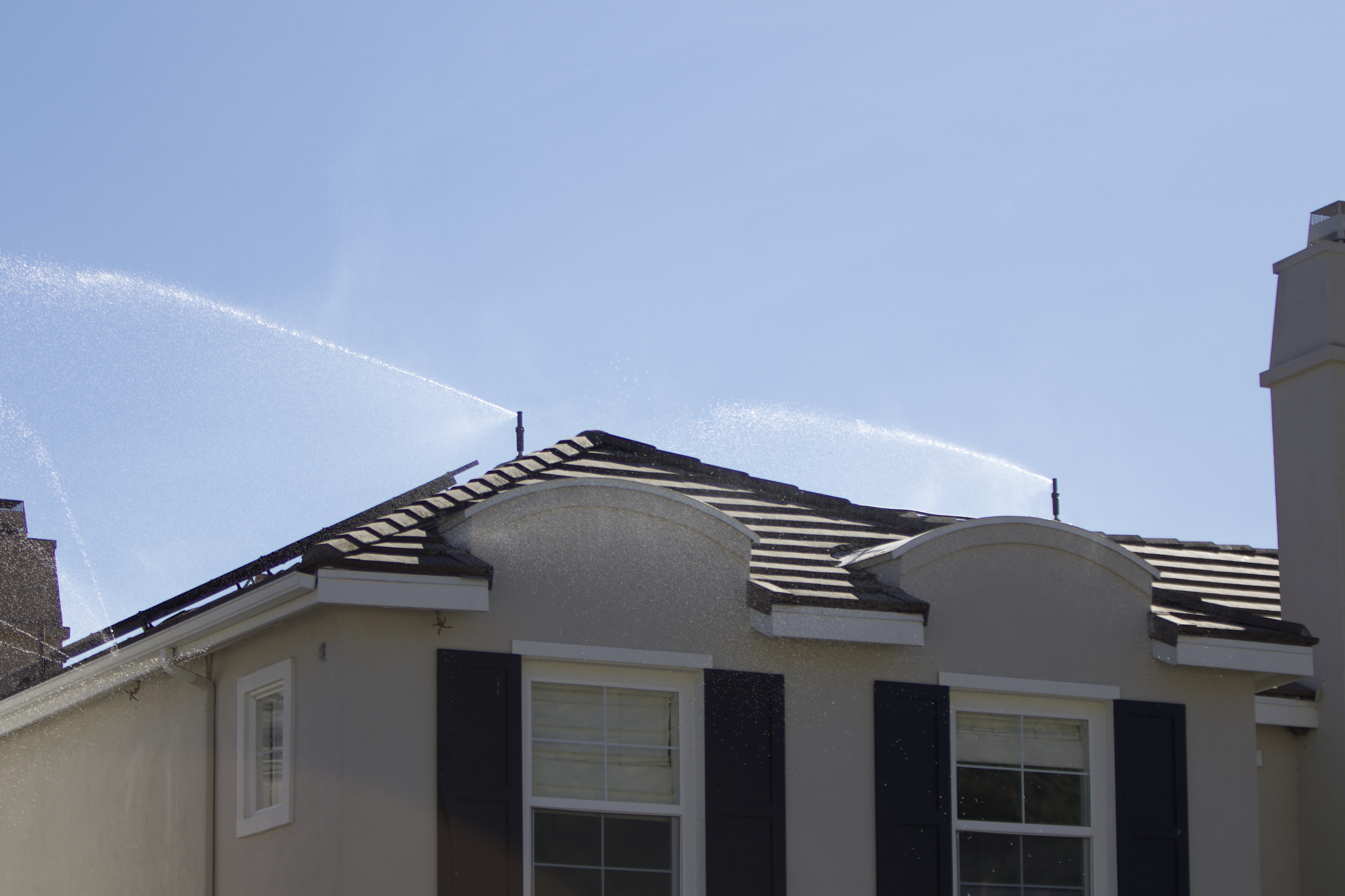 Wildfire sprinkler system actively spraying water across a structure